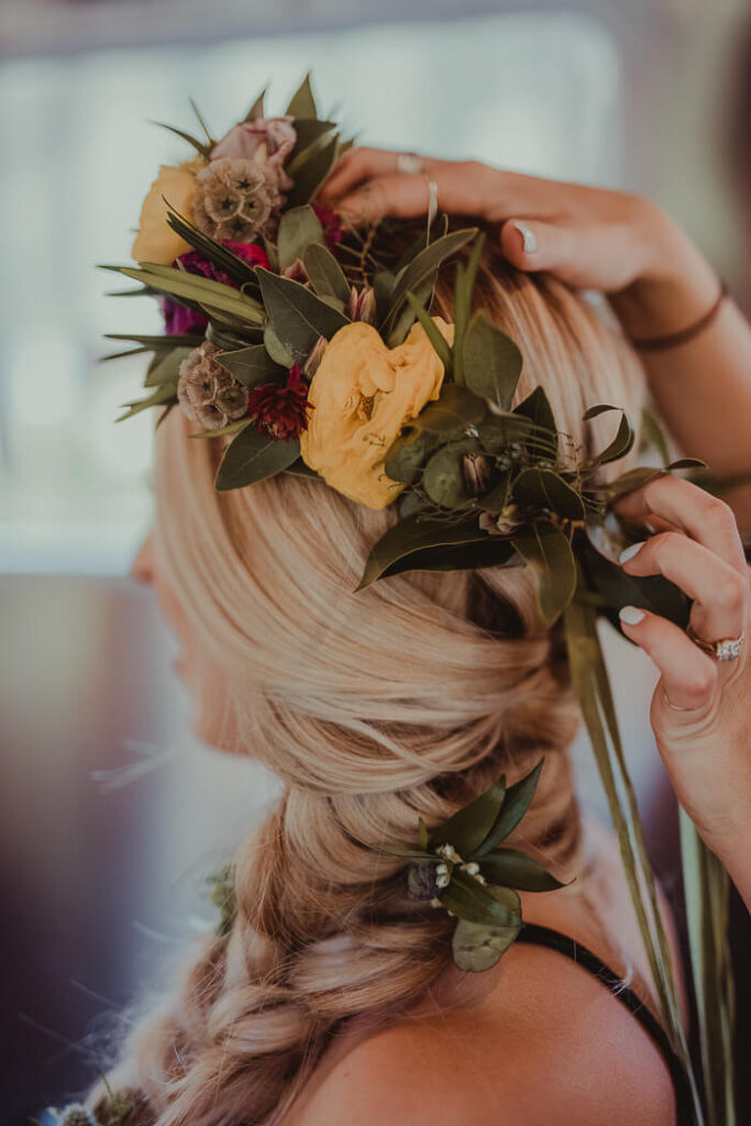 De bruid draagt als alternatief voor een bruidsboeket een bloemenkroon met gele bloemen en eucalyptus in haar losse vlecht.