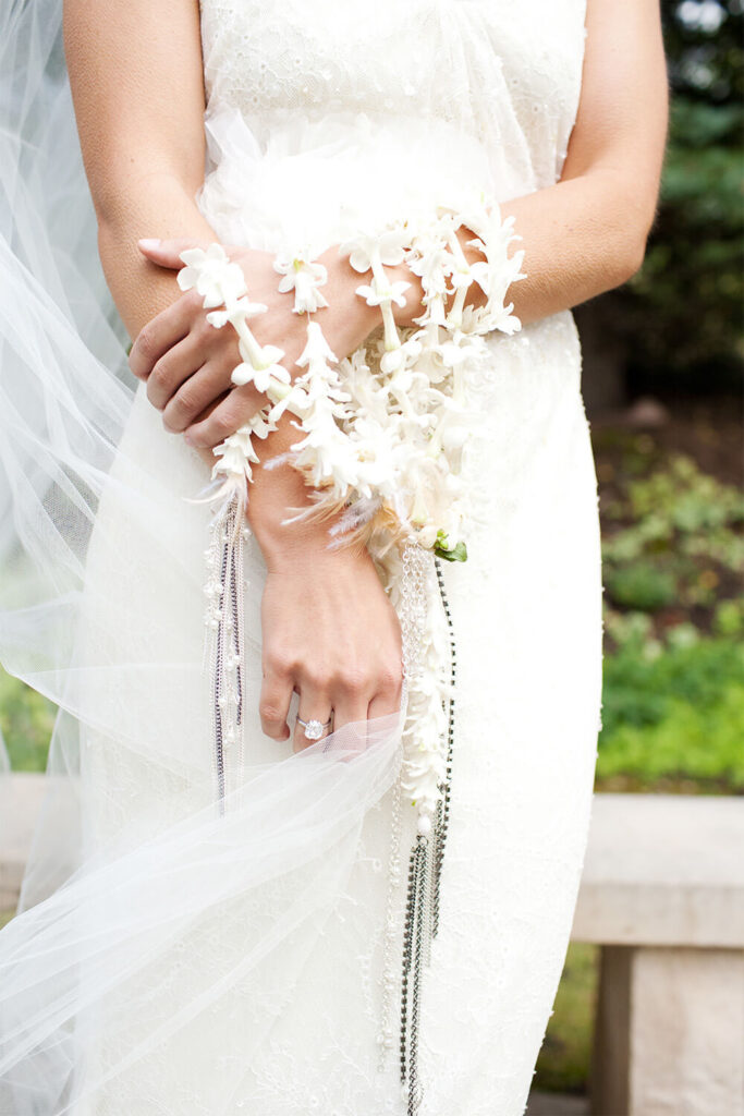 Een bruid draagt een bloemenslinger van kleine, witte bloemetjes om haar pols als alternatief voor een bruidsboeket. 
