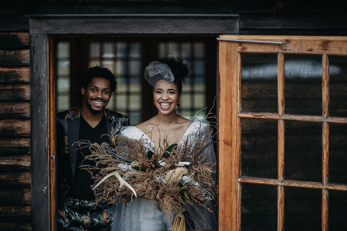 Het bruidspaar staat in een houten deuropenning en de bruid draagt een birdcage en een bos takken als alternatief van een bruidsboeket. 