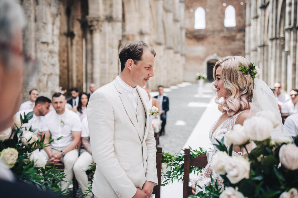 Ceremonieboekje kerkelijk huwelijk: bruidegom in beige pak en bruid met bloemen in het haar geven elkaar het jawoord. 
