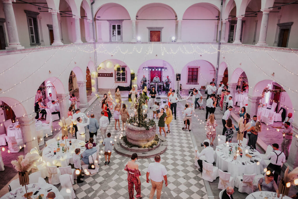 Prachtige feestlocatie met lampjes en ronde tafels waarbij huwelijksgasten dansen op de dansvloer.
