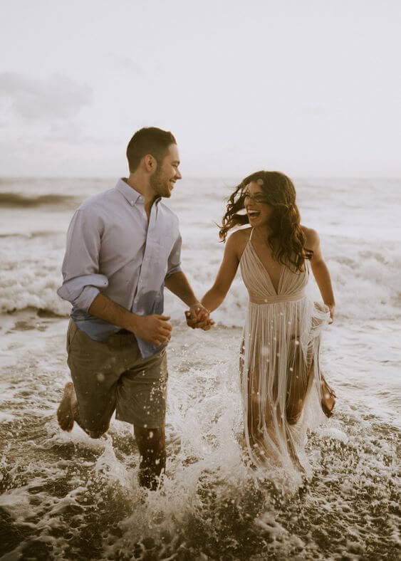 Bruid en bruidegom lachen uitbundig nadat ze met hun trouwkleding in zee gegaan zijn voor een trash the dress. 
