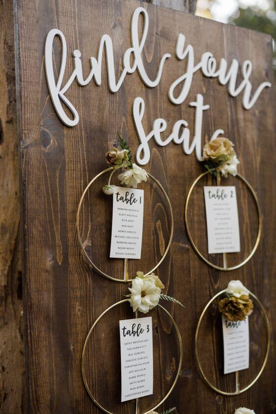 Rustiek seating plan op je bruiloft met goudkleurige loops en droogbloemen per tafel. 