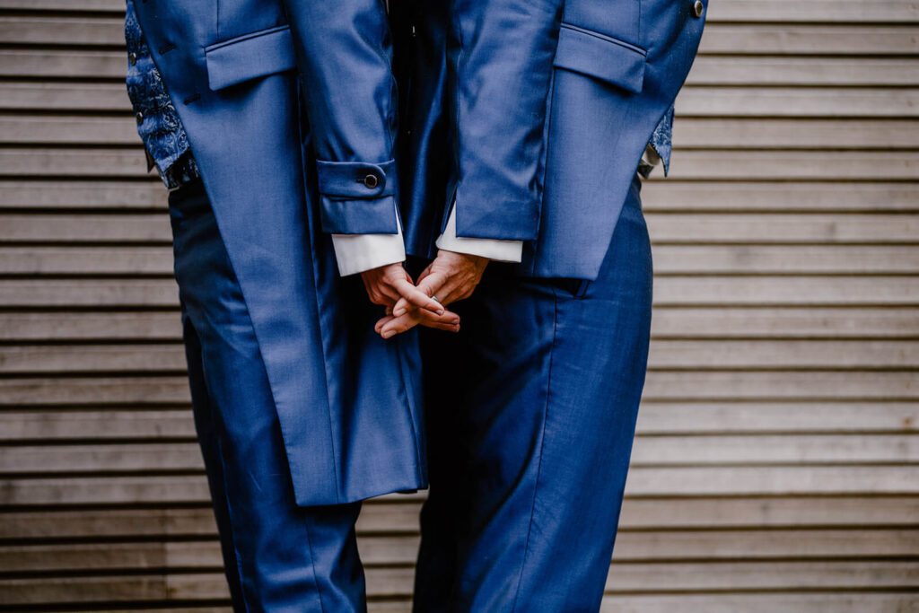 Een kostuum voor de bruidegom: homokoppel draagt kobaltblauw maatpak en houdt de handen vast. 