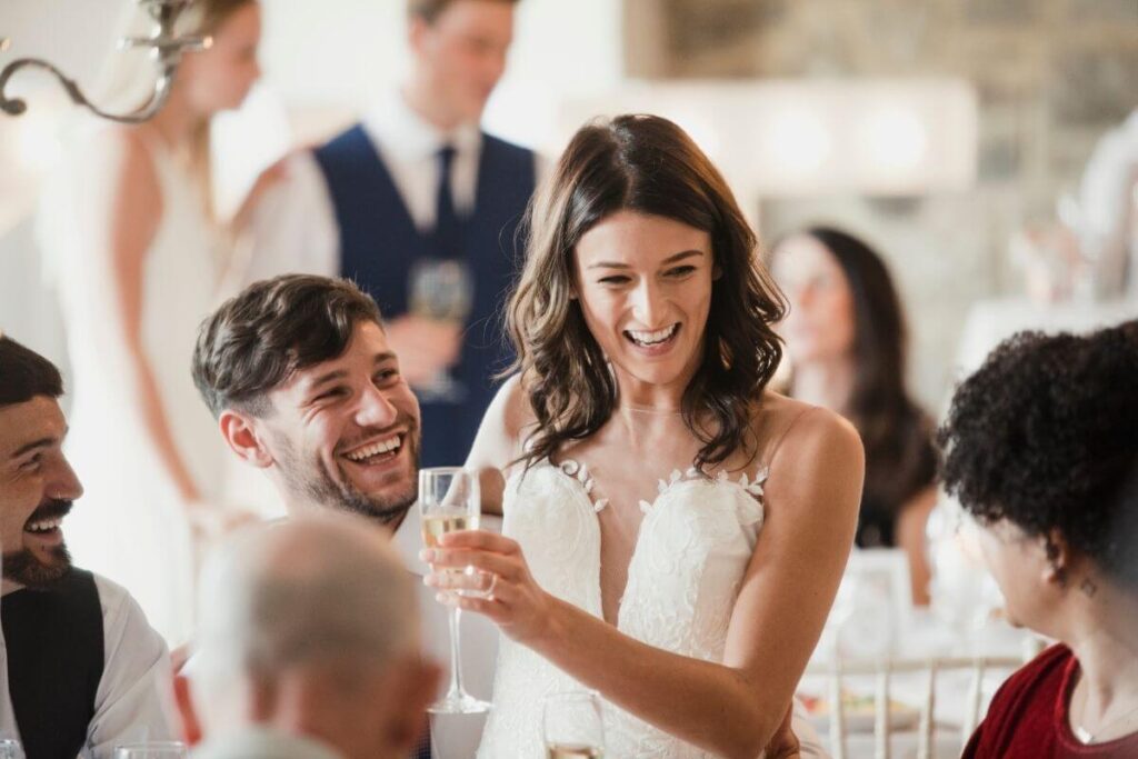 Gasten bezighouden op bruiloft: de bruid met champagne en bruidegom zitten aan tafel met hun gasten en lachen met de trouwquiz. 