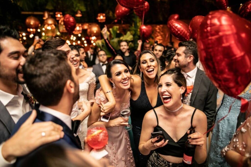Gasten bezighouden op bruiloft: de twee bruidegoms zijn omringd door hun huwelijksgasten die rode ballonnen in hartvorm vasthebben.  