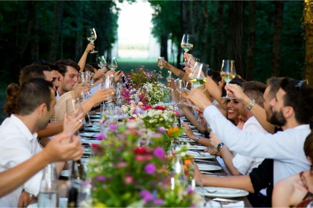 Gasten bezighouden op bruiloft: de huwelijksgasten zitten aan een lange tafel op een zomerbruiloft en klinken op de bruid en bruidegom.