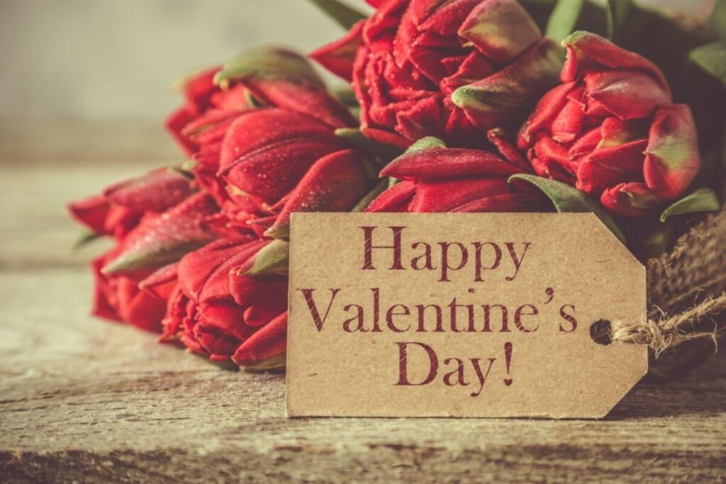 Wat doen op de eerste Valentijn als pasgetrouwd stel? Boeket rode tulpen met Valentijnskaartje ligt op houten tafel. 