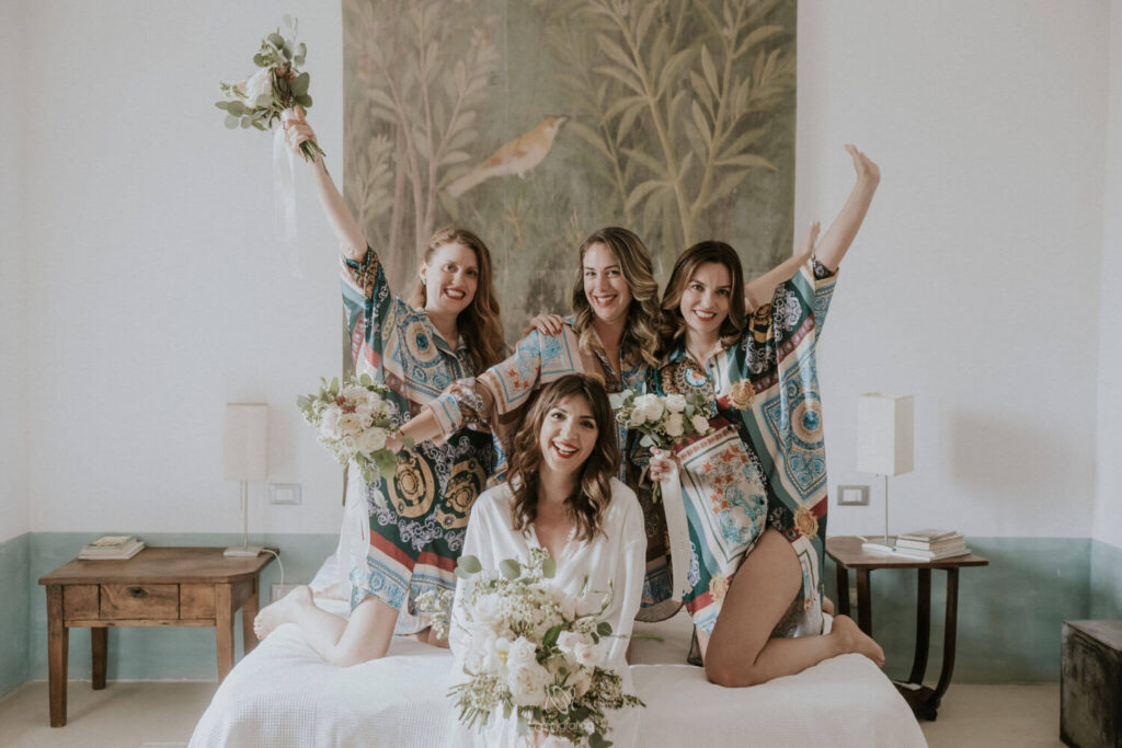 Wie nodig je uit op je bruiloft? Bruid draagt een witte kimono en zit op bed samen met haar bruidsmeisjes. 