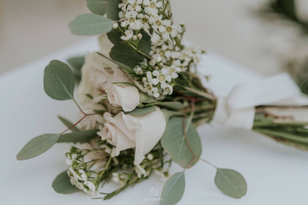 Een klein boeketje van eucalytus en witte rozen, samengebonden door een wit lint ligt sierlijk op een stoel totdat het bruidsmeisje het weer oppikt. 