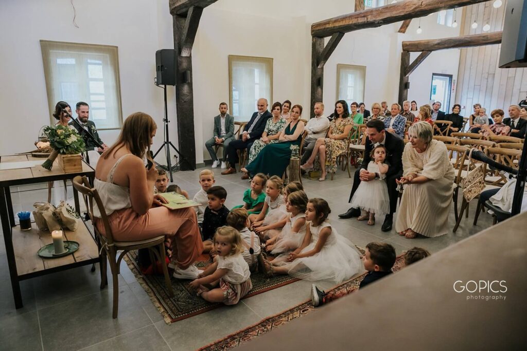 Een kleuterjuf leest voor aan alle kinderen tijdens een persoonlijke huwelijksceremonie waarbij de kinderen op een mat zitten. 