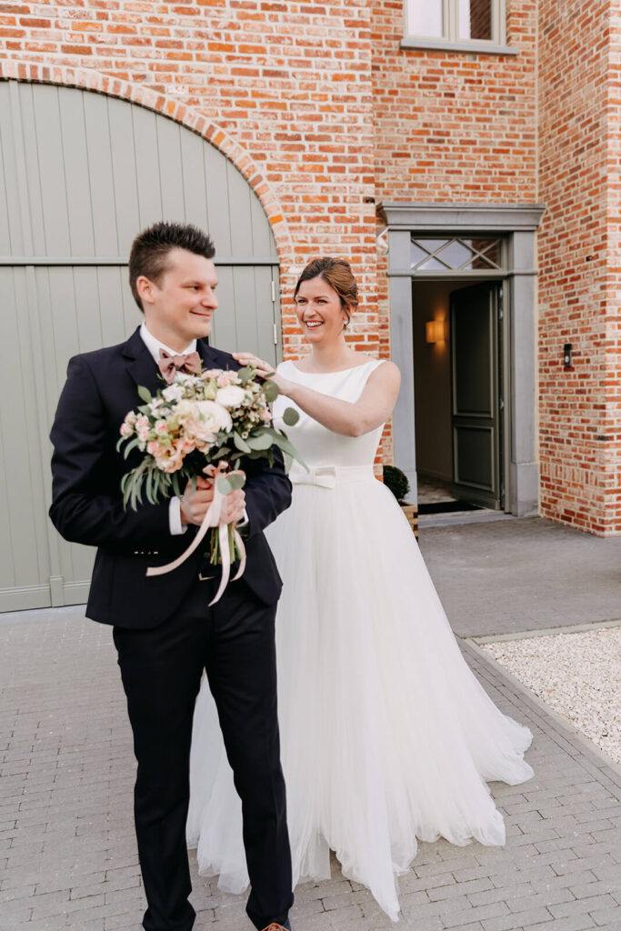 Trendy huwelijksvideo waarbij bruid in witte lange jurk en bruidegom in zwart maatpak met een mooi bruidsboeket, elkaar voor de eerste keer zien aan de voordeur van het huis.  