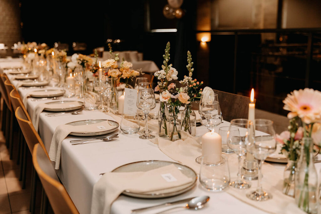 Een prachtige feesttafel kan je zelf aankleden als je goedkoper wil trouwen. Beige tafellinnen en servies en bloemendecoraties.