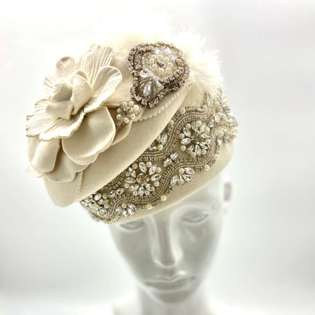 Tiara en andere haaraccessoires van het merk BrostWhyte Resurrection met een bijzonder hoedje versierd met parels, veren en briljanten en een grote 3d-bloem aan de zijkant. 