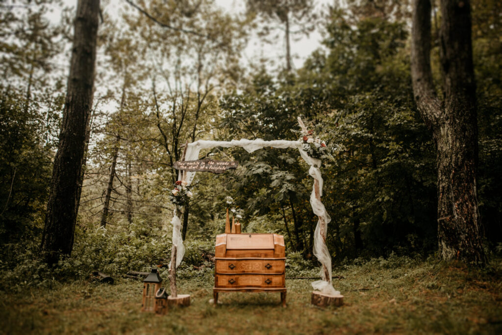 Sprookjesachtig herfsthuwelijk waarbij een romantische backdrop van hout in een bos opgesteld staat voor de huwelijksceremonie gaat beginnen. 