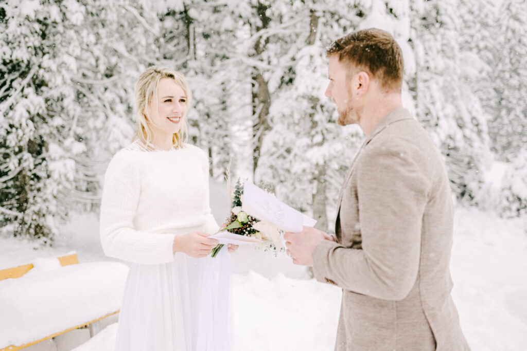Blonde bride in white wedding dress and red head groom exchanging wedding vows in the snow. 