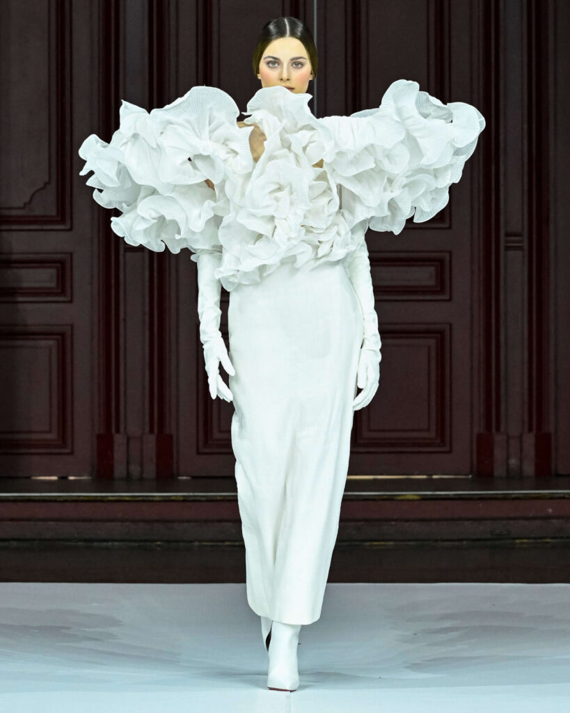 De grootste trends van Paris Haute Couture Week waarbij een model een witte opvallende schouderpartij en witte handschoenen draagt. 