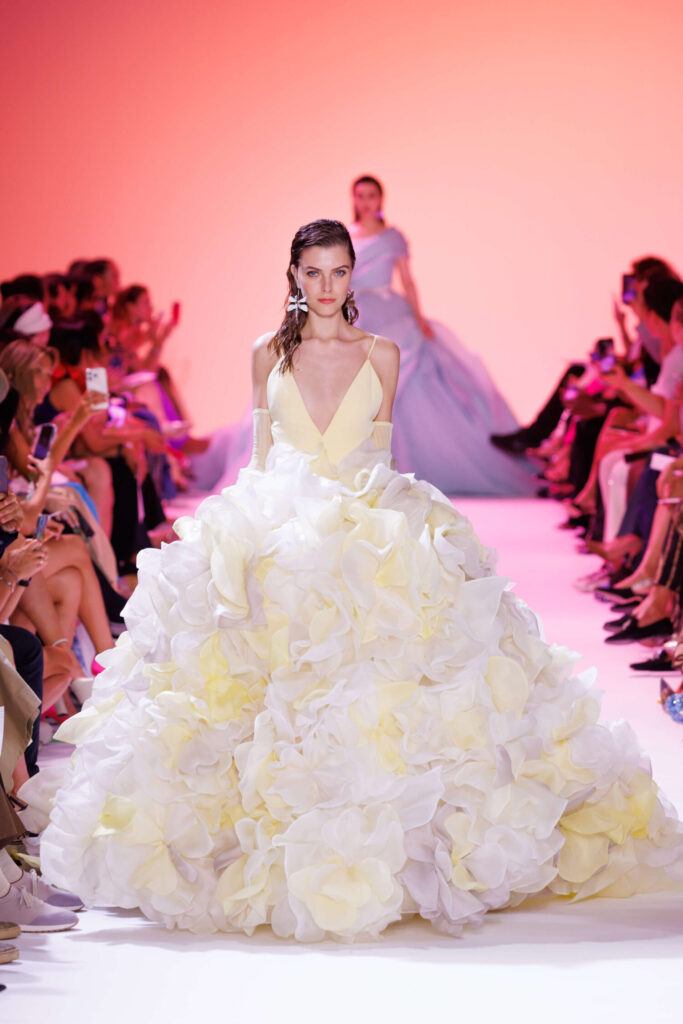 De grootste trends van Paris Haute Couture Week waarbij een model een gele baljurk draagt waarvan de rok druk bezet is met 3D-bloemen. 