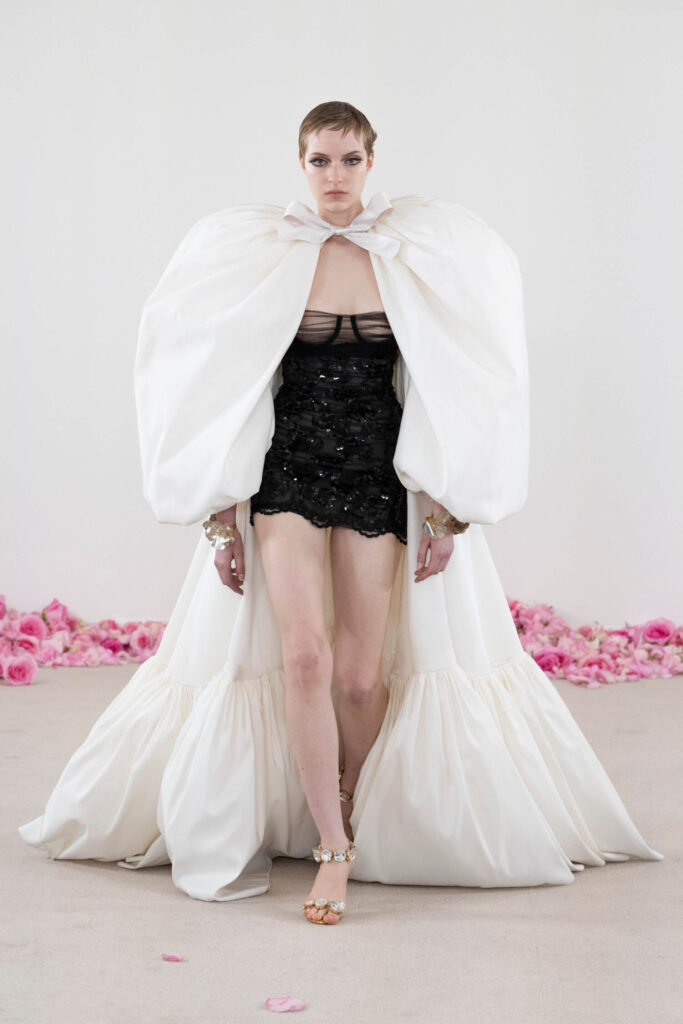 De grootste trends van Paris Haute Couture Week waarbij een model een witte cape draagt. 