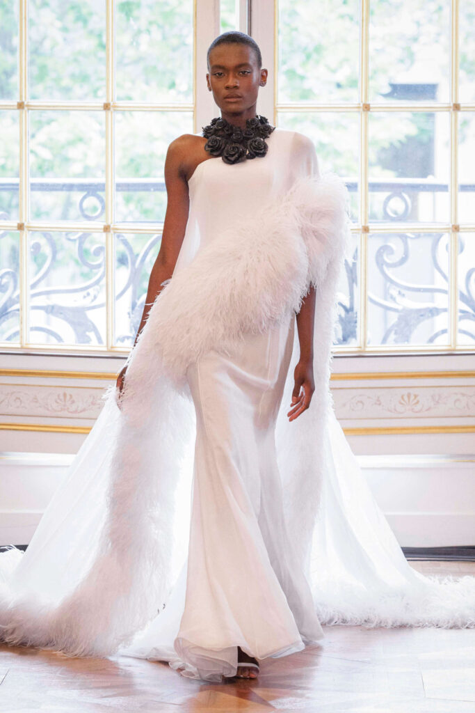 De grootste trends van Paris Haute Couture Week waarbij een model een asymetrische witte jurk met veren draagt. 